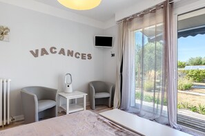 Une chambre moderne comprenant un lit, deux fauteuils, une petite table avec une lampe, un téléviseur fixé au mur et une grande fenêtre avec des rideaux.