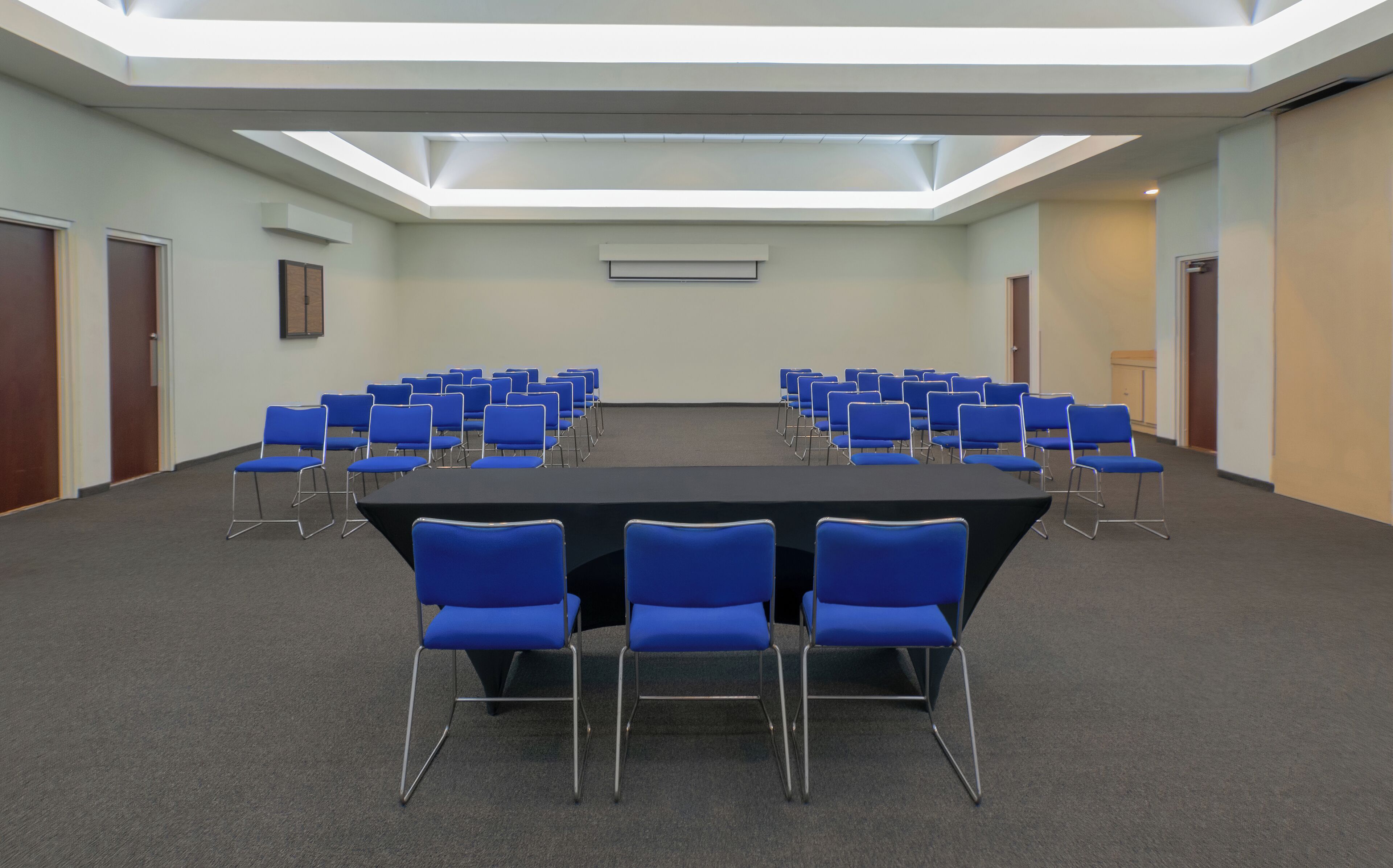 A conference room with a long table and blue chairs, a skylight, and carpeted floors.