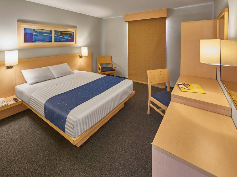 Een hotelkamer met een bed, een bureau met stoel, een telefoon en een lamp.