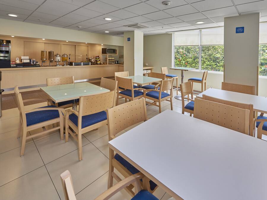 Cafetería con mesas y sillas, una máquina de café y una ventana con vista a zonas verdes.