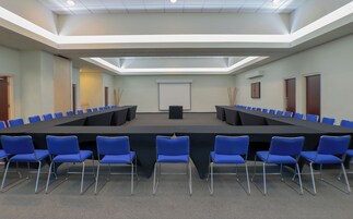 Una sala de conferencias con una mesa larga, sillas azules, una pantalla de proyector y una pizarra.