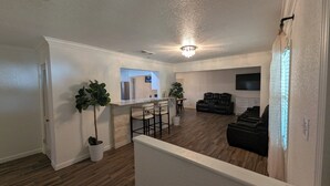 A spacious living area with a kitchen, bar stools, a seating area with couches, and a TV mounted on the wall. - 4BED Pool Down Town Home Near UMHB & SW Hospital (Belton)