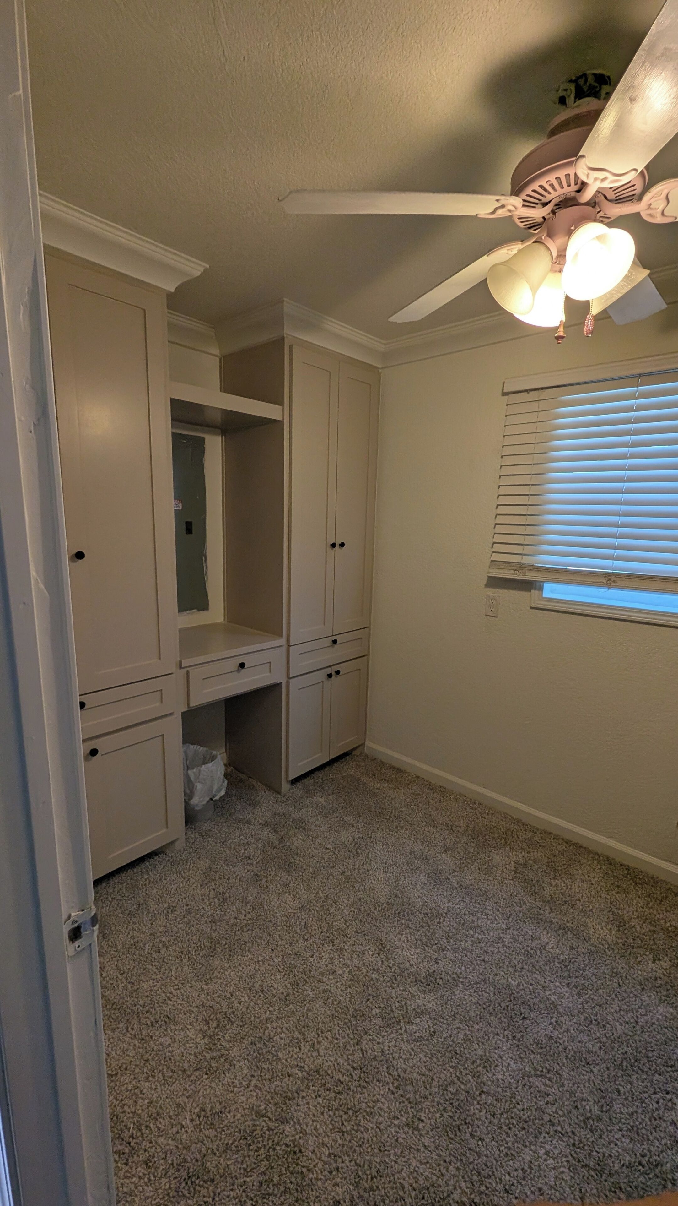 A room with a ceiling fan, a window with blinds, and a carpeted floor.