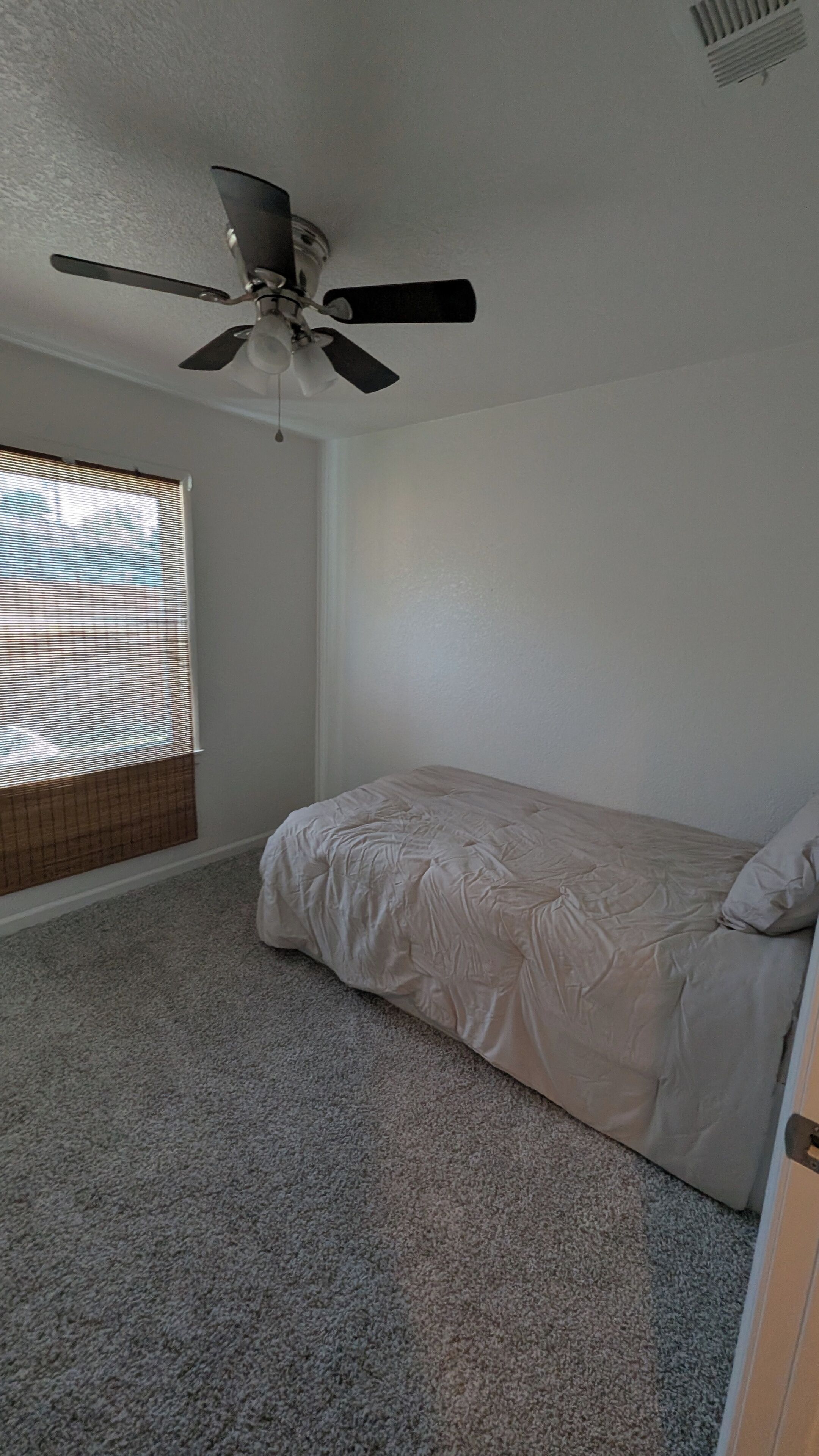 A bedroom with a bed, a ceiling fan, a window with blinds, and a carpeted floor.