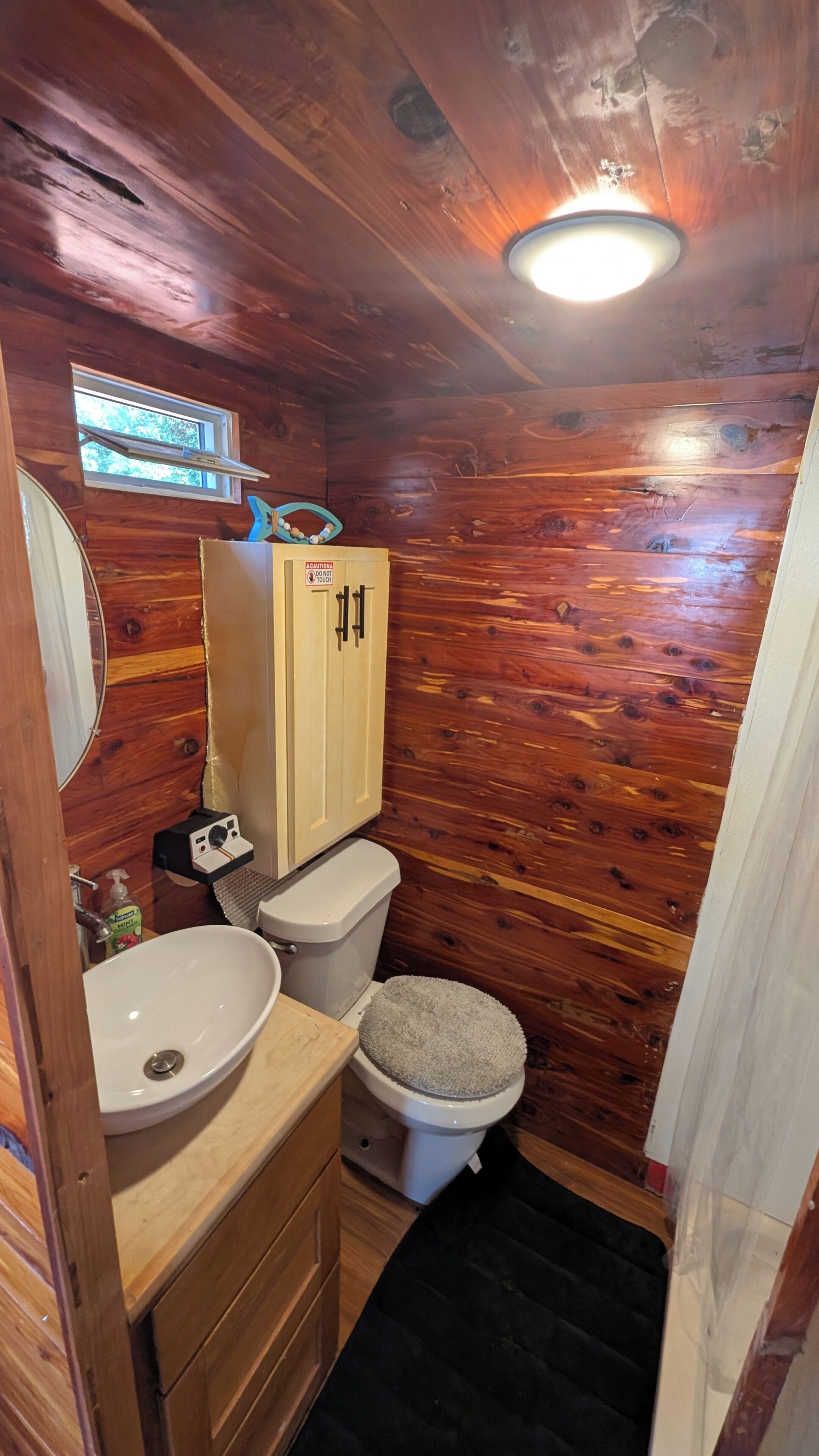 A wooden cabin bathroom with a wooden vanity, a sink, a toilet, and a window.