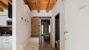 Un pasillo estrecho con una zona de cocina a un lado, un muro de ladrillo y una puerta que da a otra habitación.