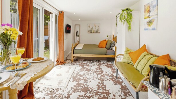 A room with a bed, a sofa, a dining area with a table and chairs, and a TV mounted on the wall.