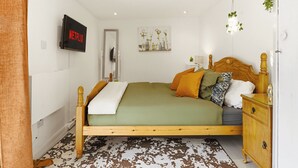 A bedroom with a bed, a dresser, a mirror, a wall-mounted TV, and a door.
