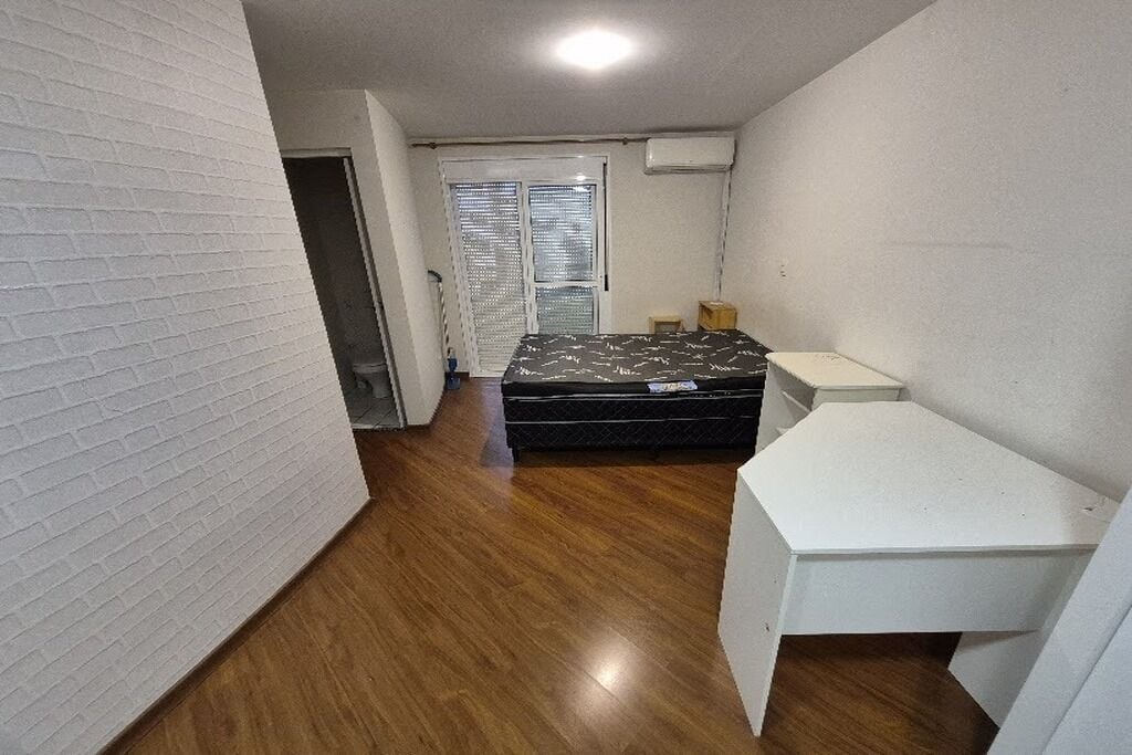 Een kleine, praktische kamer met een bed, bureau en raam met jaloezieën.