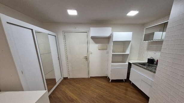 Ein Zimmer mit Holzboden, weißen Wänden, einer weißen Tür und einem weißen Schrank mit Regalen.