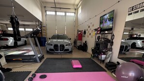 Ein Fitnessraum mit Trainingsgeräten, einem Laufband und einem Auto im Hintergrund.