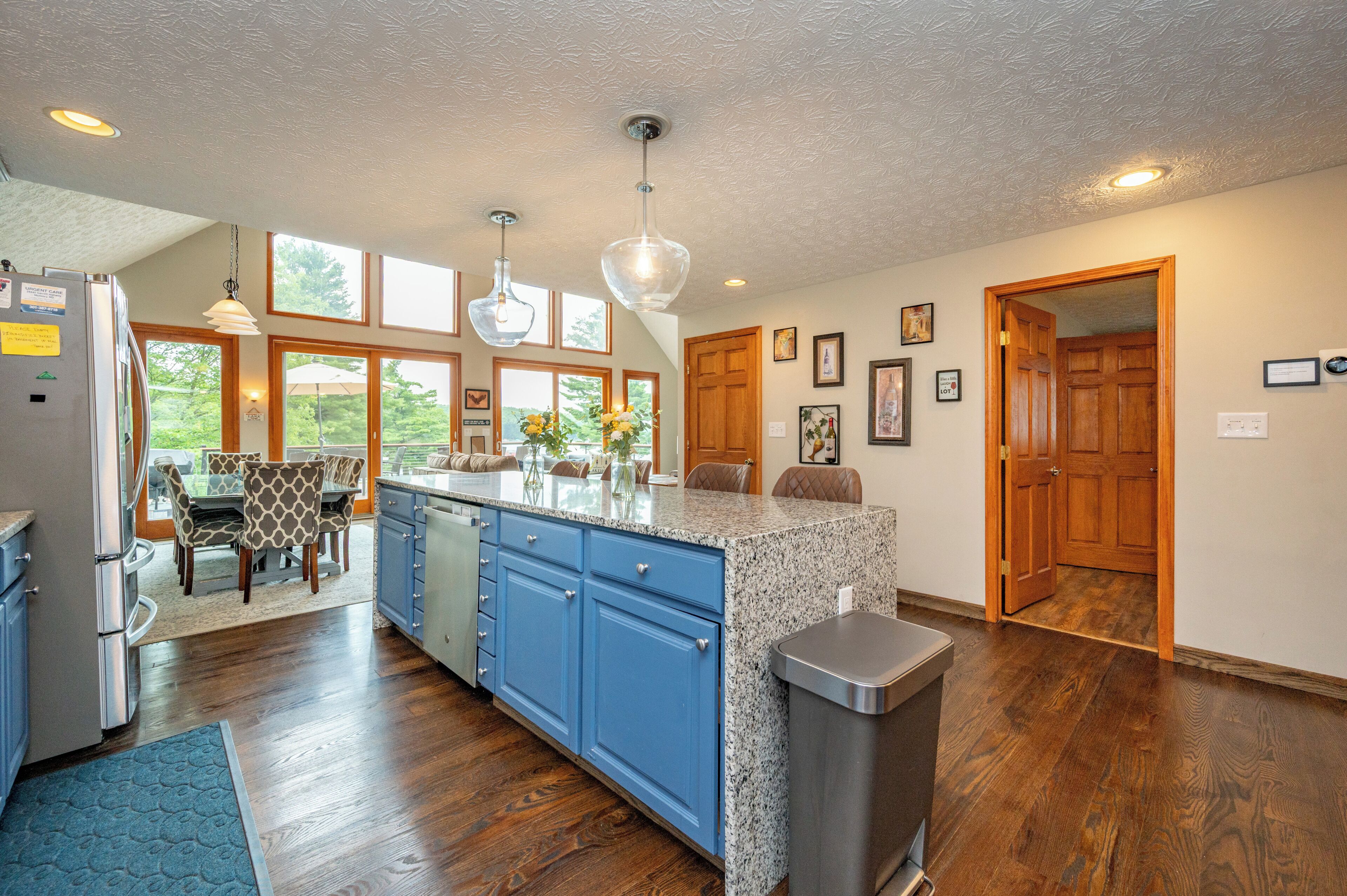 A kitchen with a granite countertop, blue cabinets, a stainless steel trash can, and a dining area with a table and chairs.