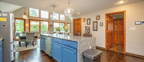 A kitchen with a granite countertop, blue cabinets, a stainless steel trash can, and a dining area with a table and chairs.