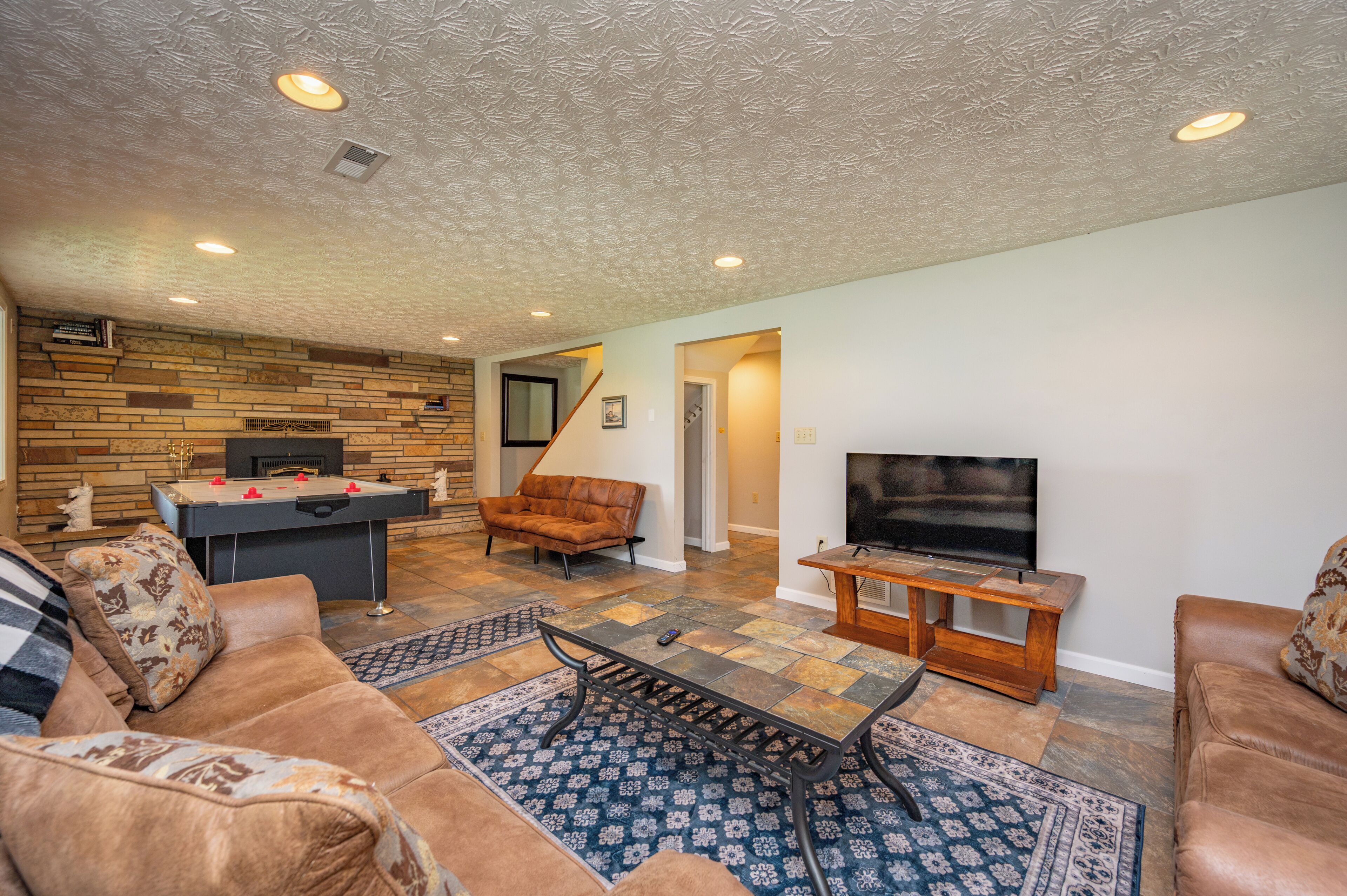 A living room with a foosball table, leather sofas, a television, and a patterned rug.