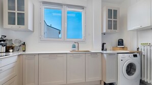 Una cucina moderna con lavatrice integrata, mobili bianchi e una finestra che si affaccia su un edificio.