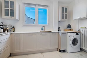 A modern kitchen with a built-in washer, white cabinetry, and a window with a view of a building. - Air-conditioned Apartment with 2 Suites & 2 Balconies near the Beaches (Cagnes-sur-Mer)