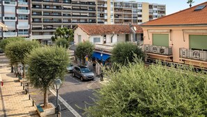 Una veduta di una strada con file di edifici residenziali, un'auto parcheggiata e un piccolo negozio con tenda blu.