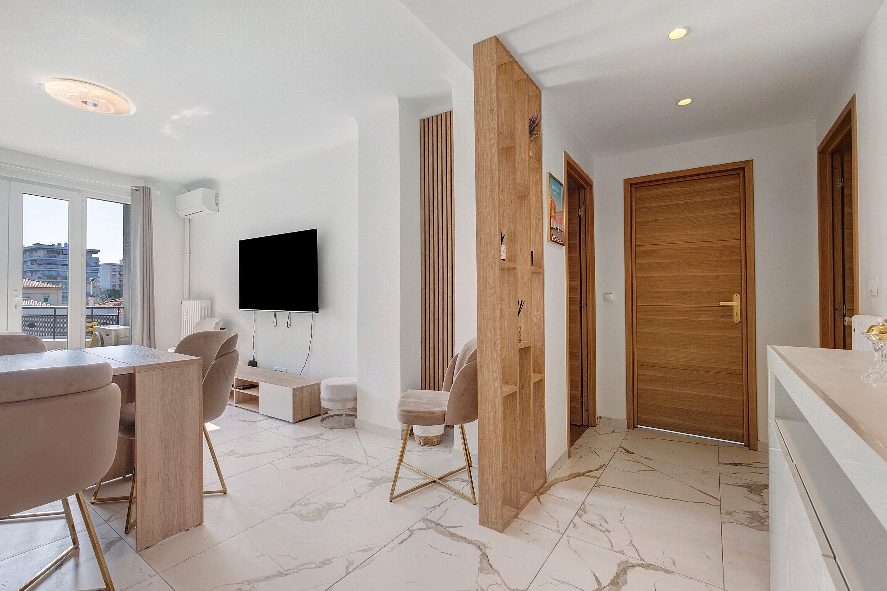 Un salón moderno con un televisor de pantalla plana, una zona de comedor con mesa y sillas, y vistas de la ciudad a través de grandes ventanales.