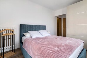 A bedroom with a bed, a radiator, a wooden hanger, and a wardrobe. - Air-conditioned Apartment with 2 Suites & 2 Balconies near the Beaches (Cagnes-sur-Mer)