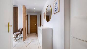 A hallway with a white wall, a wooden door, a white counter, and a chair.