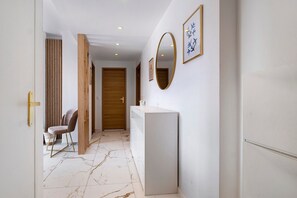 A hallway with a white wall, a wooden door, a white counter, and a chair. - Air-conditioned Apartment with 2 Suites & 2 Balconies near the Beaches (Cagnes-sur-Mer)