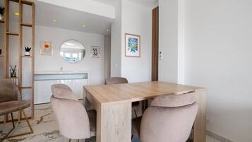 A modern dining area with a wooden table and four chairs, a kitchen in the background, and a mirror on the wall.