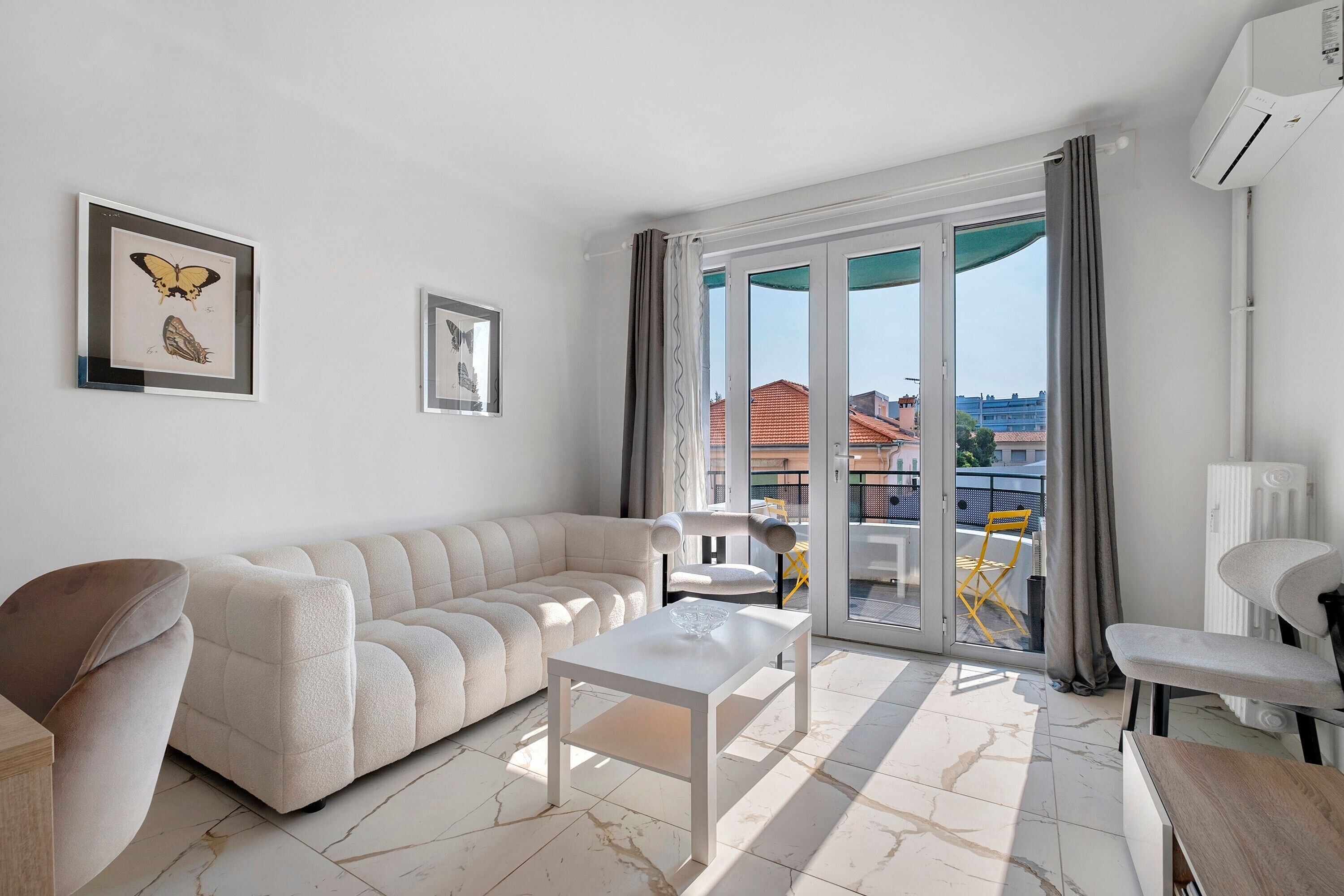 A modern living room with a sofa, a coffee table, and a balcony with a view of buildings.