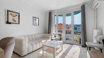 A modern living room with a sofa, a coffee table, and a balcony with a view of buildings.