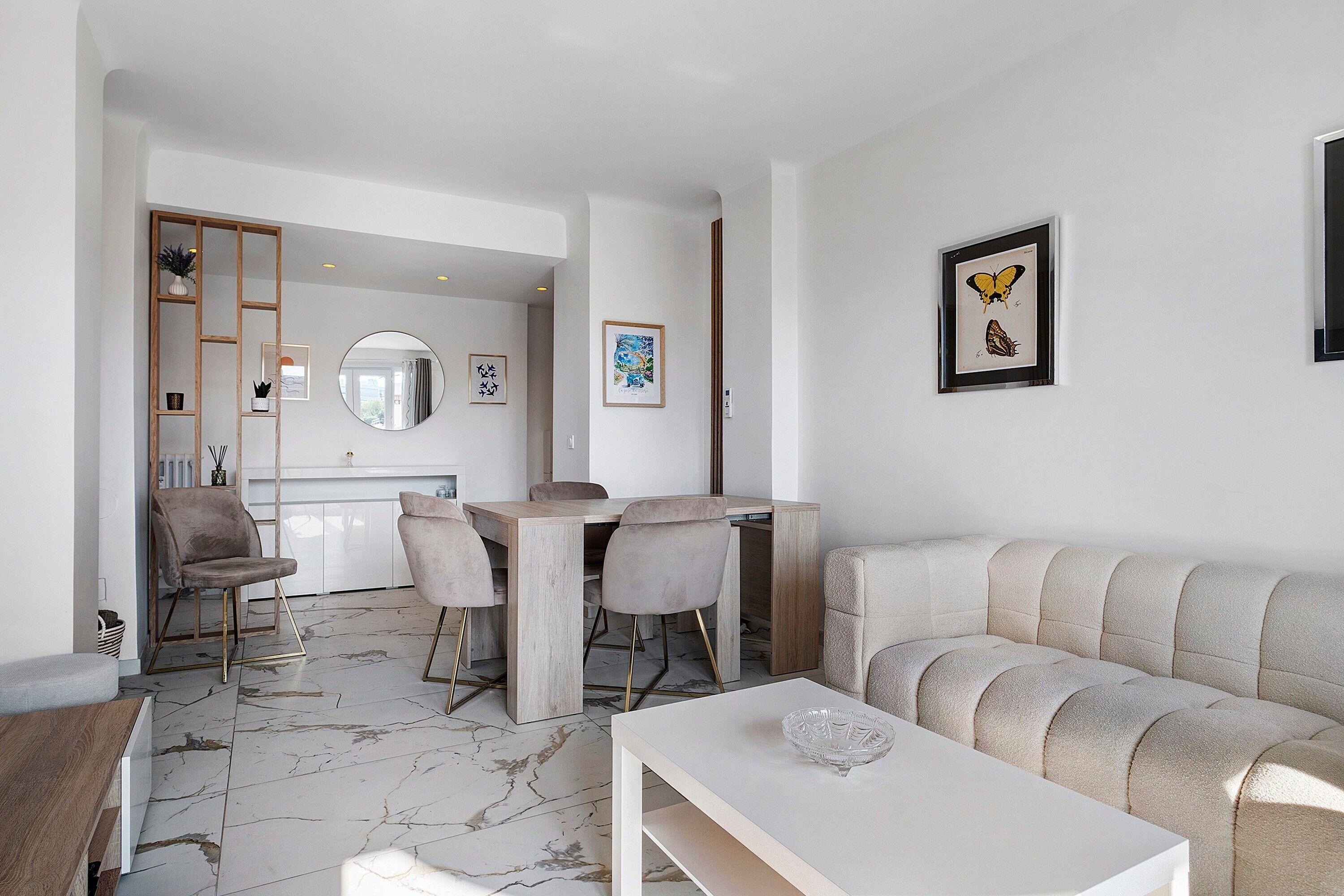 Ein modernes Wohnzimmer mit Marmorboden, einem weißen Sofa, einem Esstisch mit Stühlen und Kunstwerken an den Wänden.