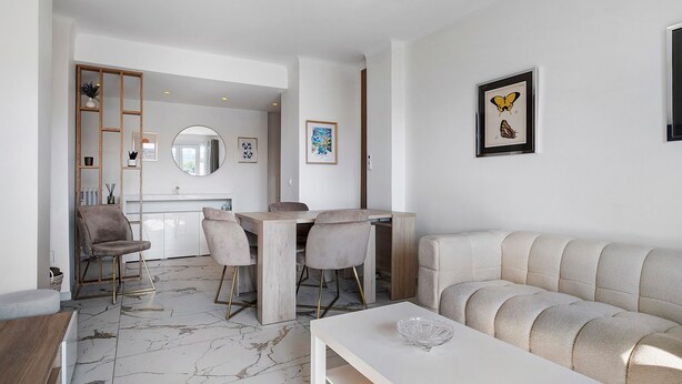 Un soggiorno moderno con pavimento in marmo, un divano bianco, un tavolo da pranzo con sedie e opere d'arte alle pareti.