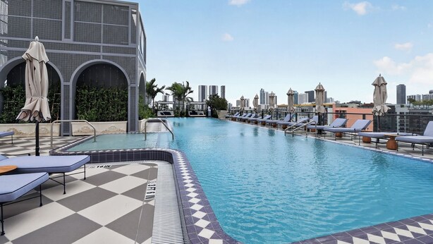 Piscina en la azotea con sillas de descanso, piso a cuadros y vistas a la ciudad.