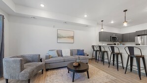 Una sala de estar moderna con sofá, sillones, una mesa de centro y una zona de cocina con taburetes de bar.