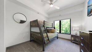 Un dormitorio con literas, ventilador de techo, un ventanal grande y un aparador.