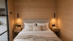 Een moderne slaapkamer met een houten plafond, een groot bed met een beige deken, twee nachtkastjes met lampen, en een groot raam.