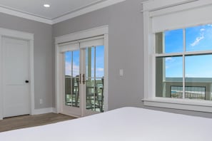 A bedroom with a large window, a door, and a view of the beach. - Windward Crest (Port St. Joe)