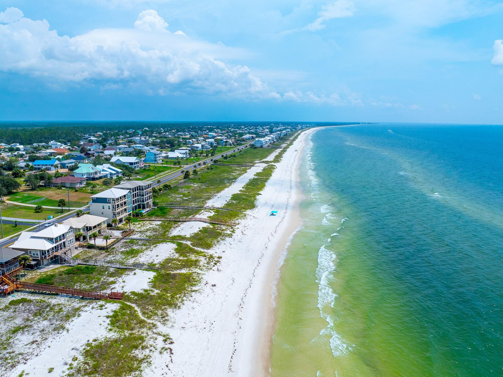 Un pueblo costero con una extensa playa de arena, un océano azul cristalino y una hilera de casas a lo largo de la costa.