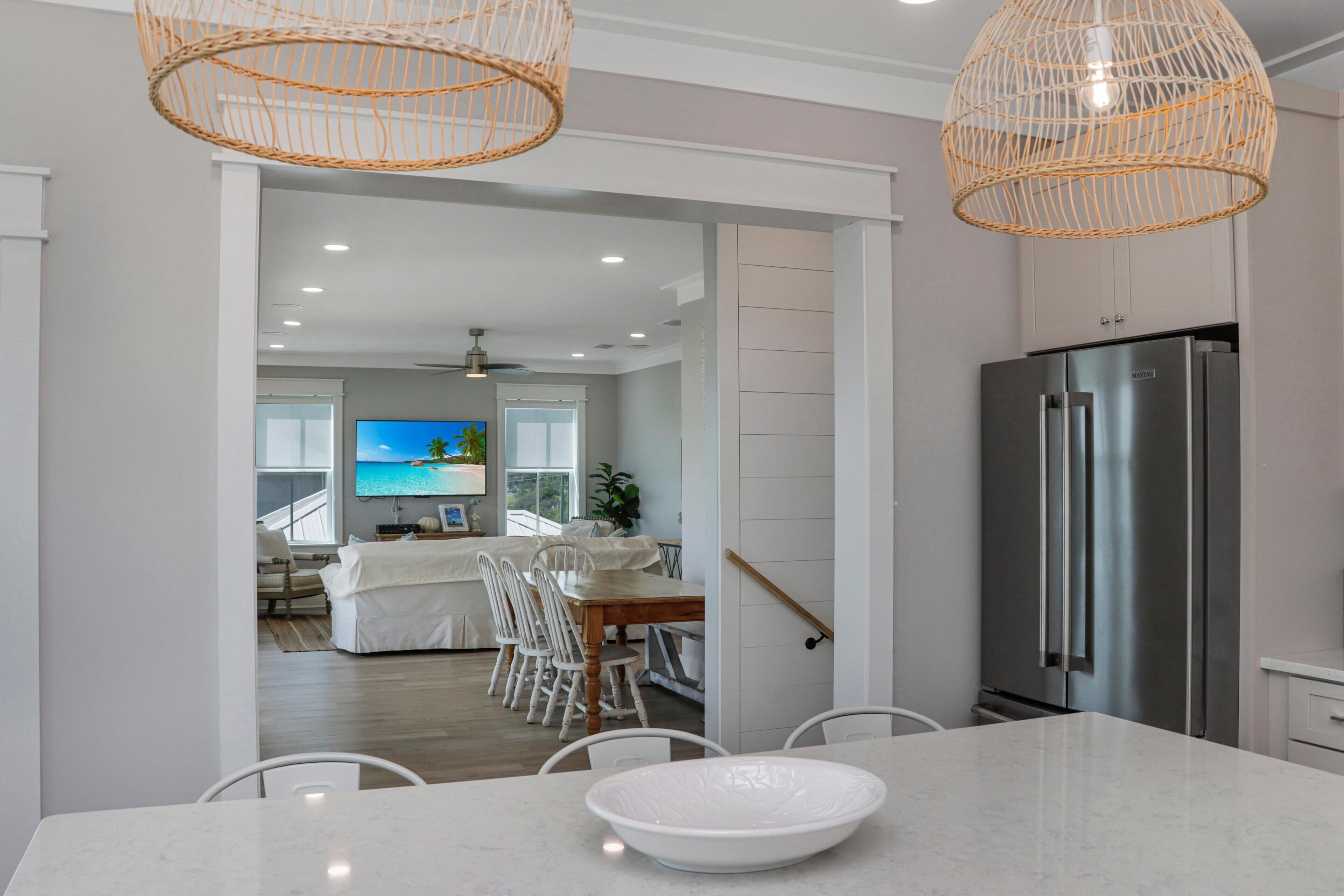 A modern kitchen with a large stainless steel refrigerator, a dining area with a white table and chairs, and a living room with a television.