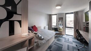 A modern hotel room with a bed, desk, chair, and a view through a large window. - Student Only The View (Newcastle)