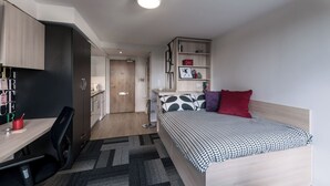 A compact bedroom with a bed, bedside table, and a desk with a chair. - Student Only The View (Newcastle)