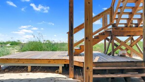 Una terraza de madera con vista a la playa y las dunas.