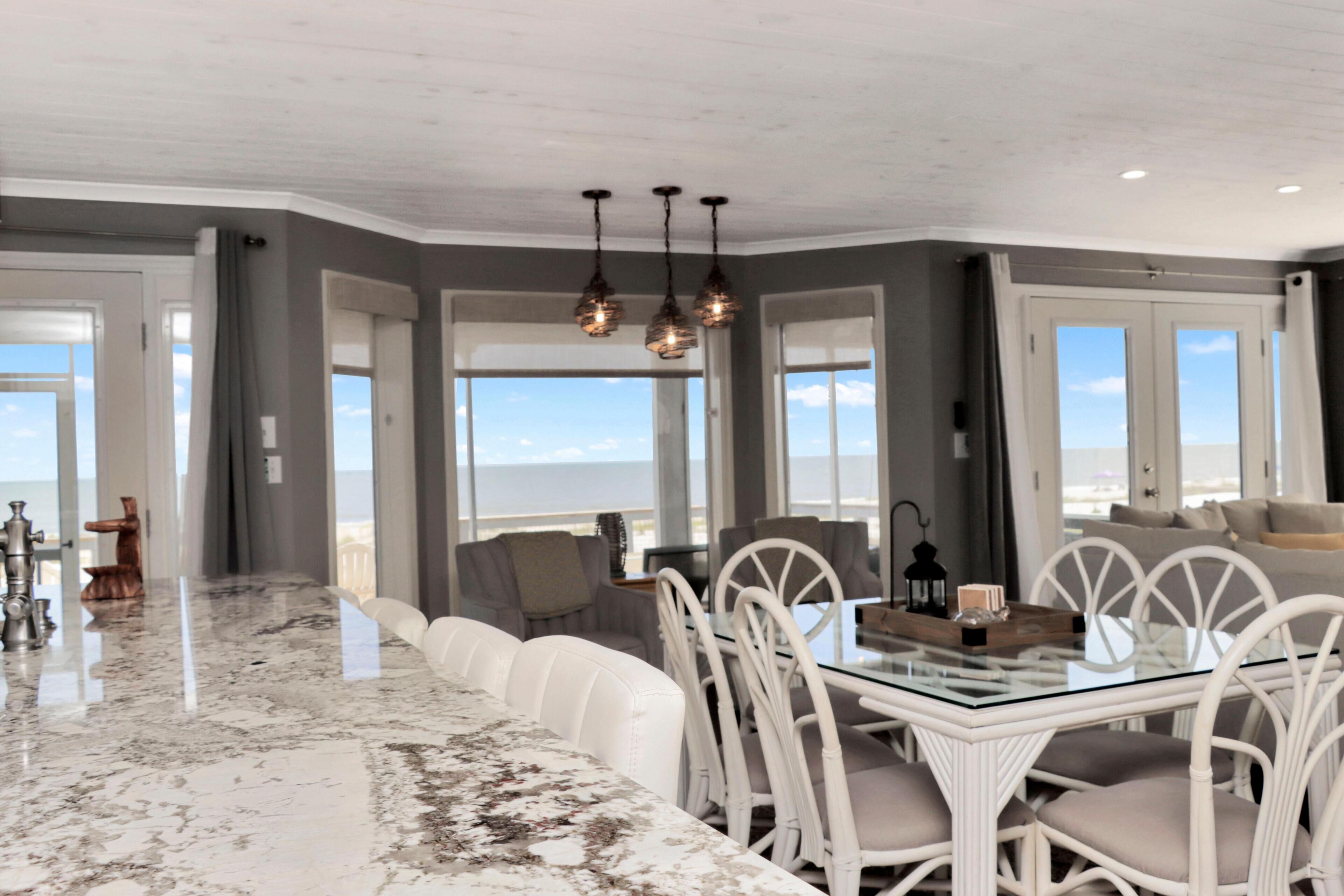 Un comedor moderno con una mesa de vidrio, sillas blancas y vista al océano.
