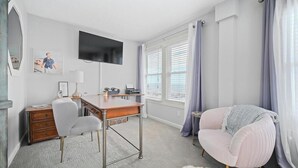 Una habitación con escritorio, silla, televisor y ventana con cortinas.