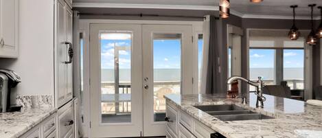 A kitchen with a large island, stainless steel appliances, and a view to the outside.