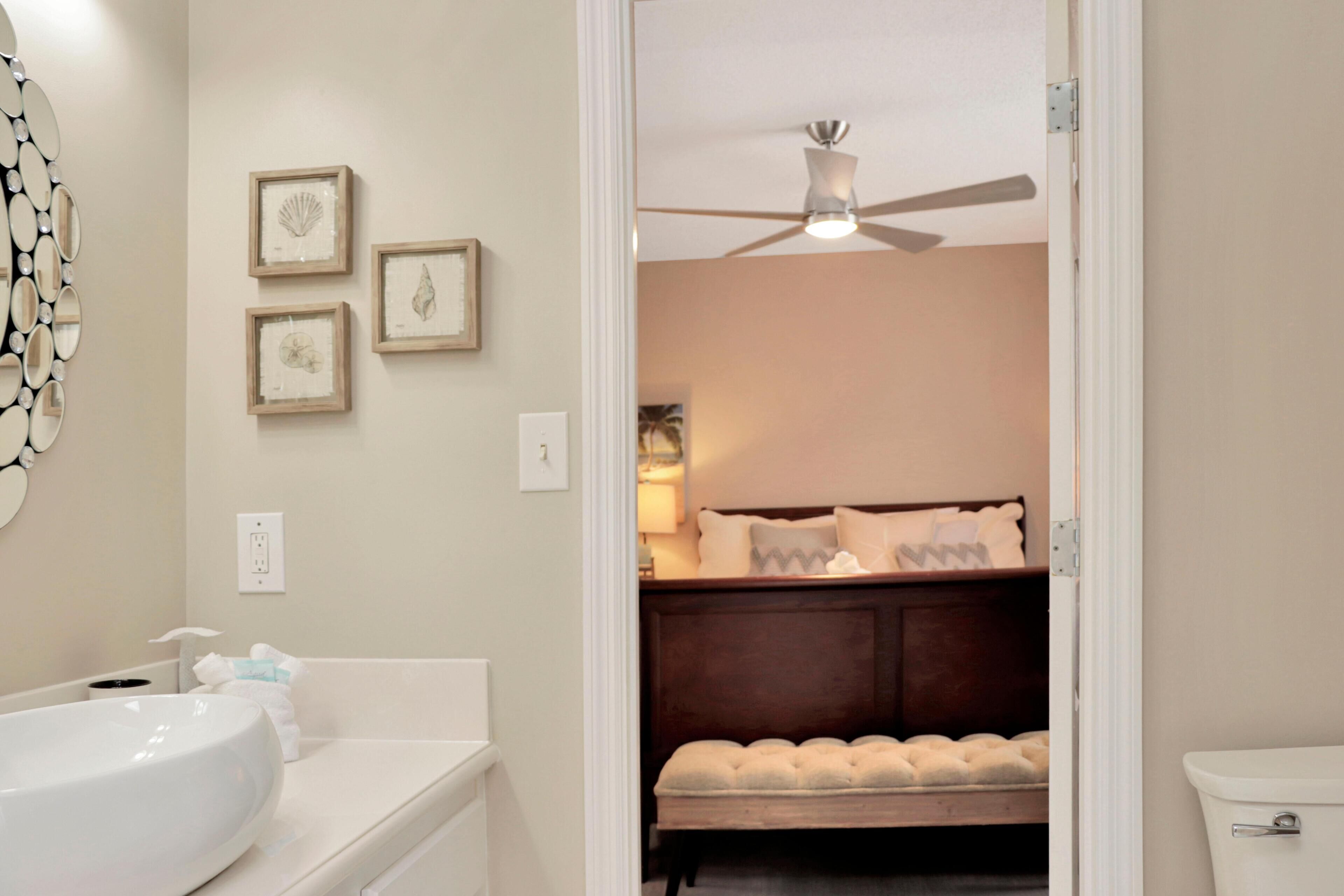 Une salle de bain avec un lavabo blanc, un ventilateur de plafond et des tableaux encadrés accrochés au mur.