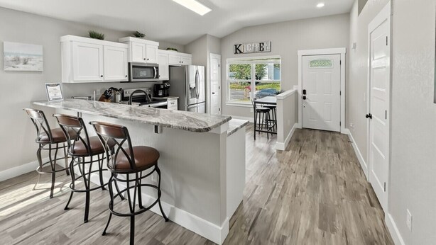 A modern kitchen with white cabinetry, a central island with bar stools, and a view to the outside. - Captain`s Quarters - New Listing (Pensacola)
