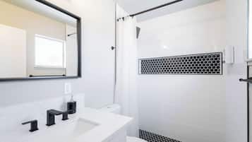 Un baño moderno con lavamanos blanco, accesorios negros, ducha con azulejos hexagonales y un espejo grande.