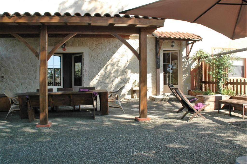 Un espacio de estar al aire libre cubierto con pared de piedra, mobiliario de madera y una pérgola.