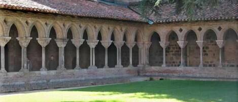 A courtyard with a series of arches and a brick building in the background.