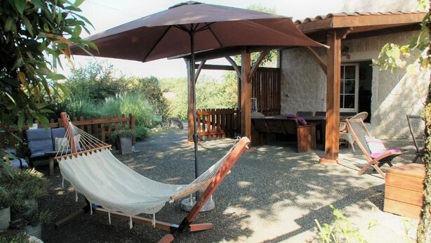 Una hamaca bajo un paraguas grande, una terraza de madera y mobiliario exterior.