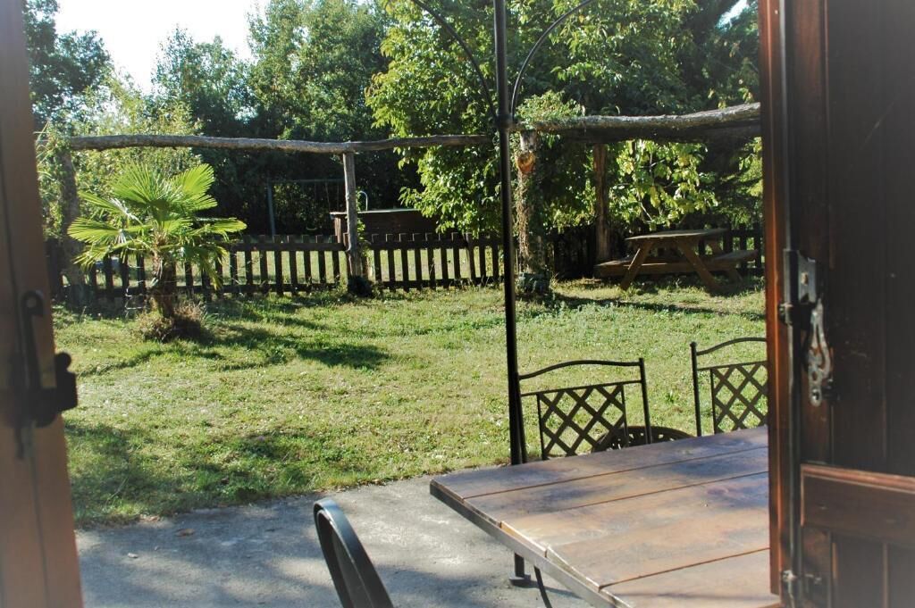 Une terrasse extérieure avec une table et des chaises, entourée d’une clôture en bois et d’arbres.